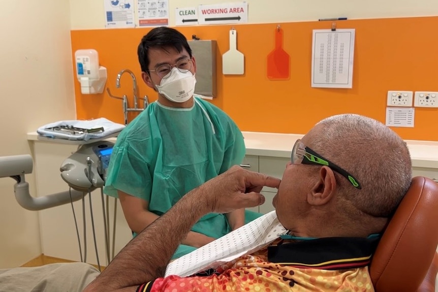 Man in scrubs talks to man in dental chair.