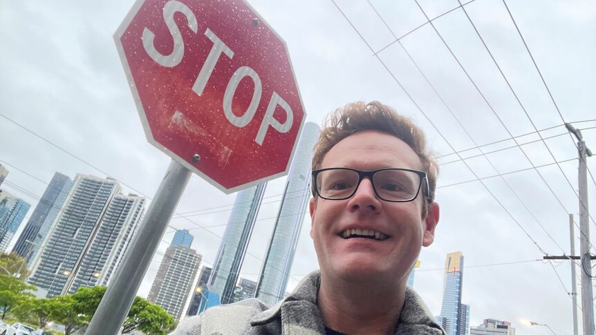 A man takes a selfie with a stop sign on a street in Southbank, Melbourne. 