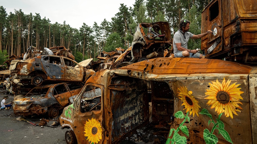 American artist Trek Thunder Kelly paints sunflowers on cars which were destroyed by Russian attack in Irpin.