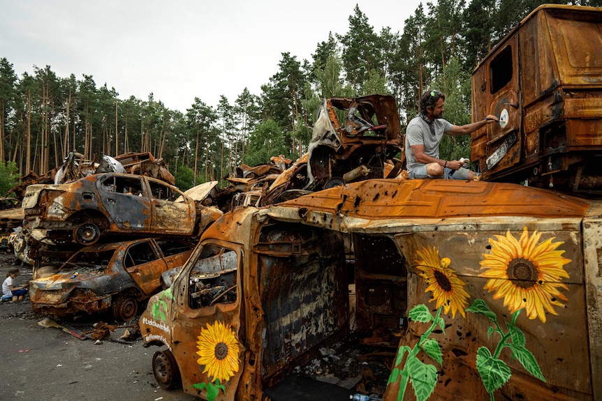 American artist Trek Thunder Kelly paints sunflowers on cars which were destroyed by Russian attack in Irpin.