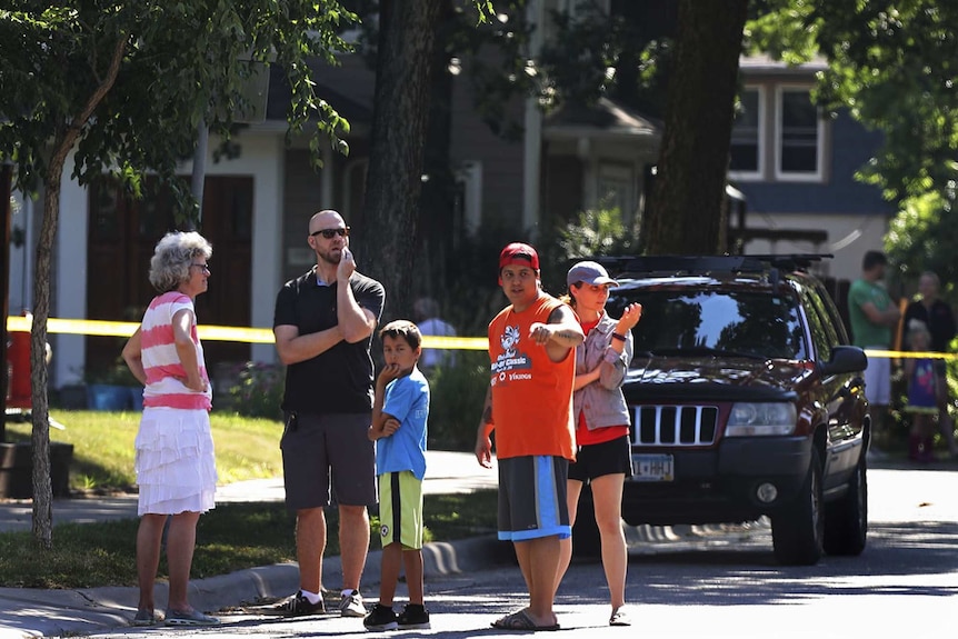 Neighbours stand confused on the sidewalk which is blocked off with yellow police tape