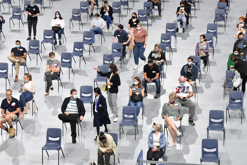 People wait in chairs at a vaccine hub.