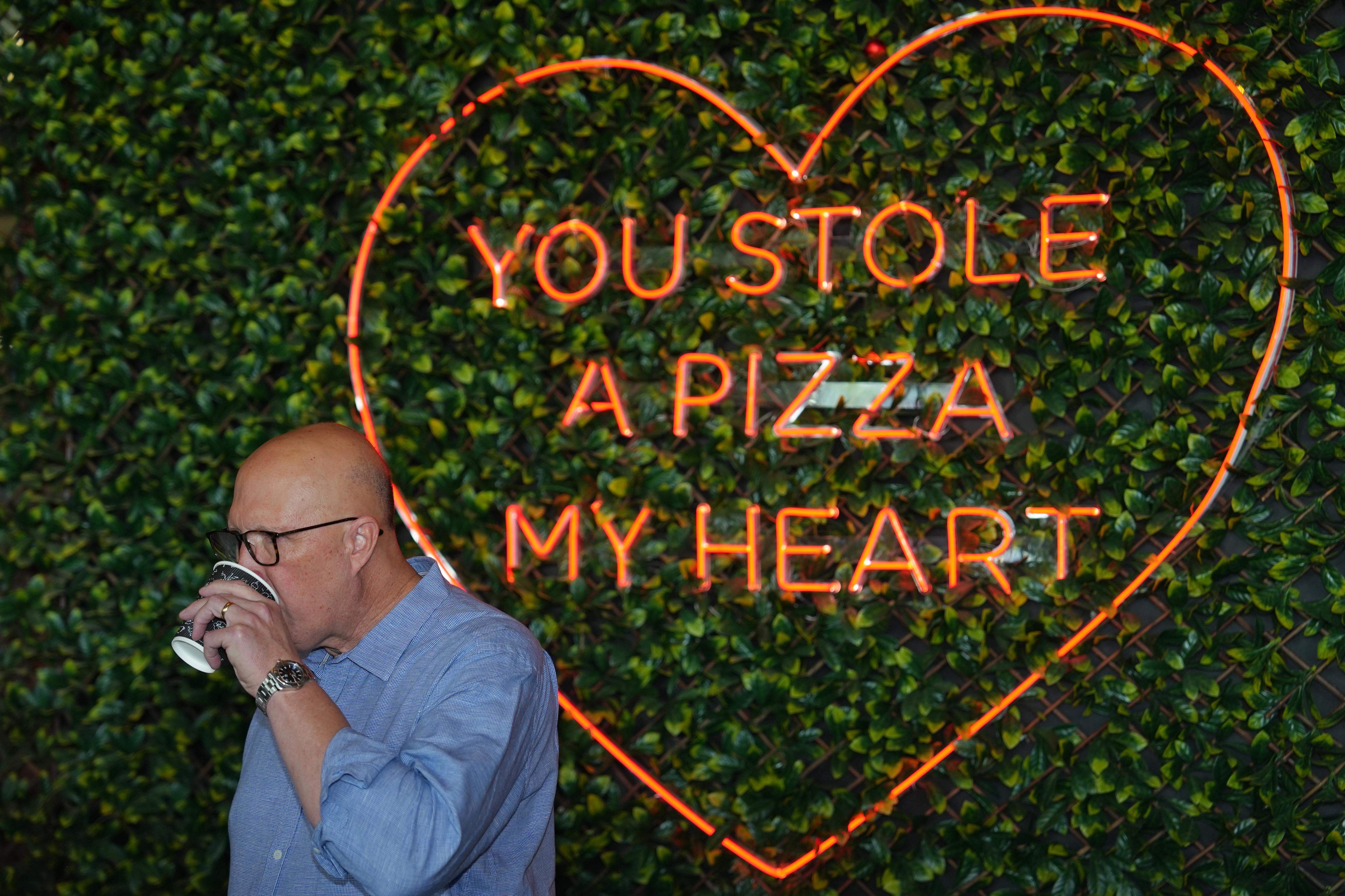 Dutton stands in front of a sign at a pizza shop saying "you stole a pizza my heart"