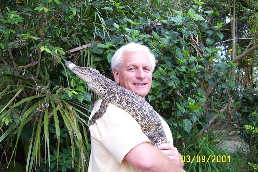 John Lever wears a khaki shirt and smiles with a young crocodile hanging over his shoulder.