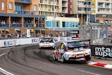 Race cars round a bend on a street circuit, lined with crowds.