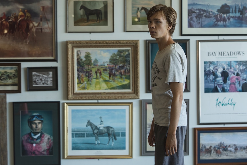 Colour still of Charlie Plummer standing in front of wall of horse artworks in 2018 film Lean on Pete.