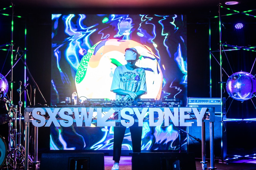 A man DJ's on a stage behind a sign that says SXSW Sydney.
