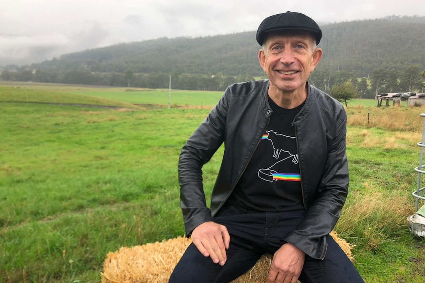 A man in a peak cap sitting on hay bale in the green Tasmanian countryside.