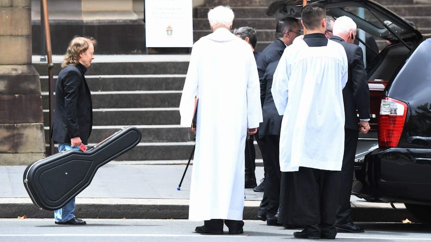 Angus Young carries a guitar to his brother's hearse after the service (Photo: AAP).