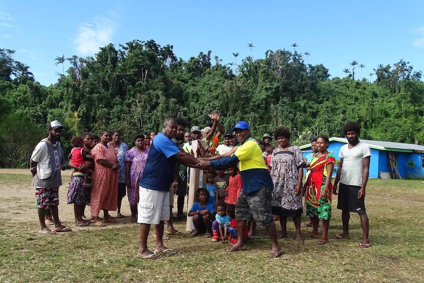 More than a dozen villagers in Vanuatu gather together, with green foliage visible in the background