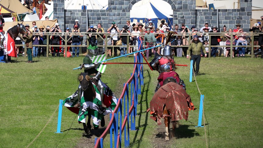 Two riders on horseback brake lances against each other's shields as the crowd looks on.