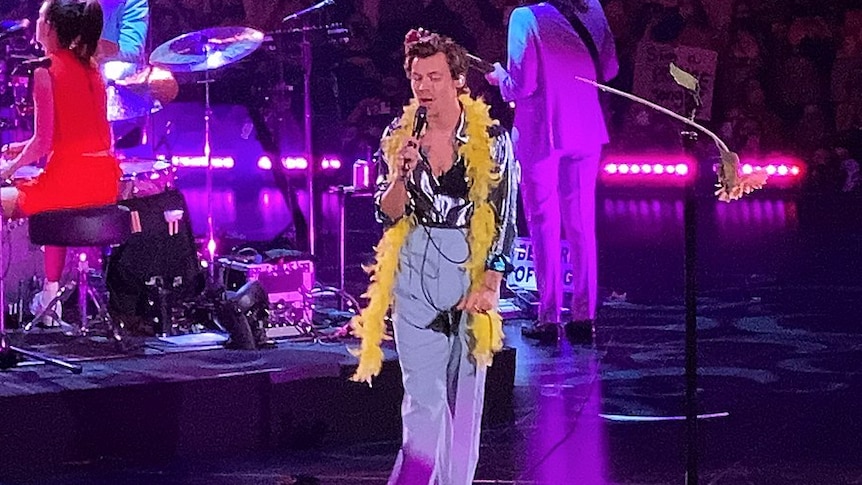 A young man on stage, wearing a yellow feather boa around his neck.