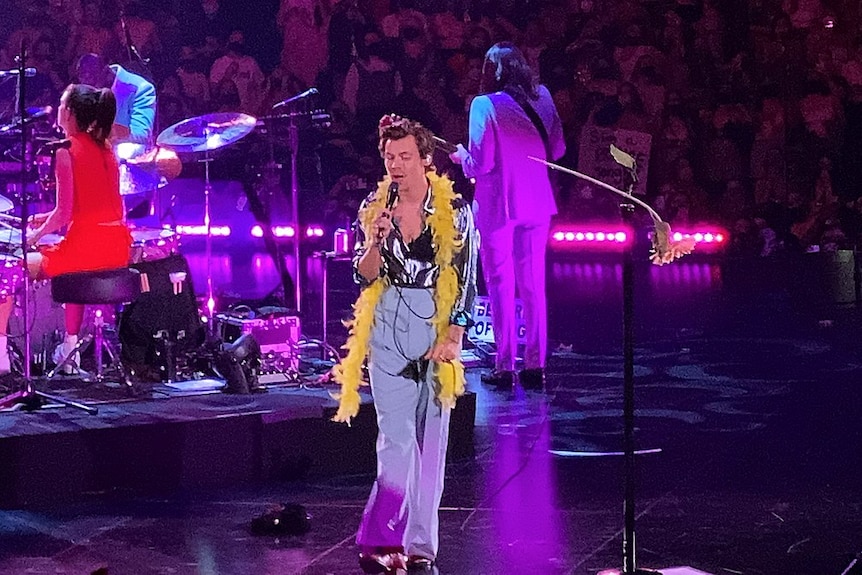 A young man on stage, wearing a yellow feather boa around his neck.