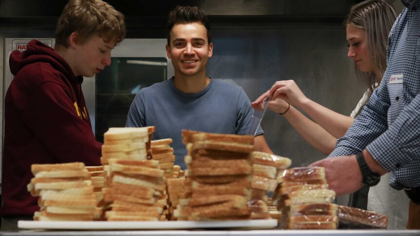 Lyndon Galea standing behind piles of sandwiches