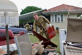 A member of the defence force carries broken furniture from a flooded home.