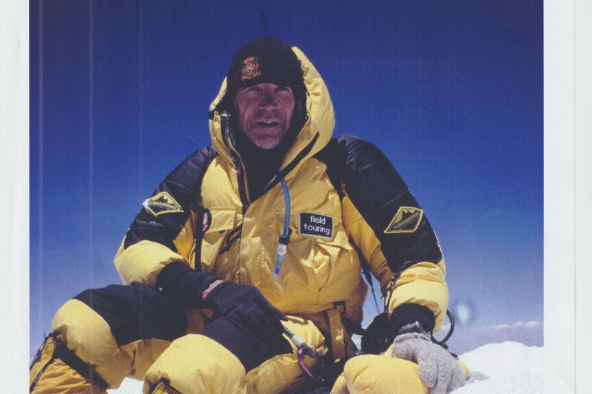 A man in a yellow and black snow suit sitting on a mountain of snow