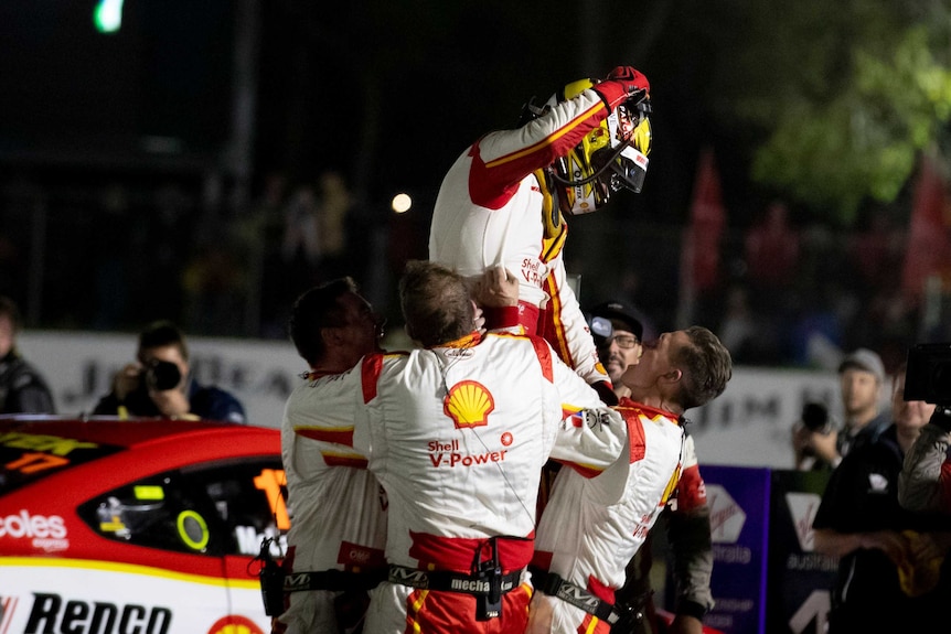 A racing driver is lifted into the air by his team mates at night