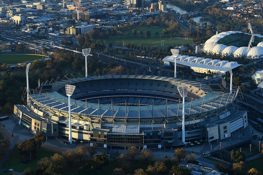 A large empty stadium seen from the sky with parkland and a smaller stadium behind it