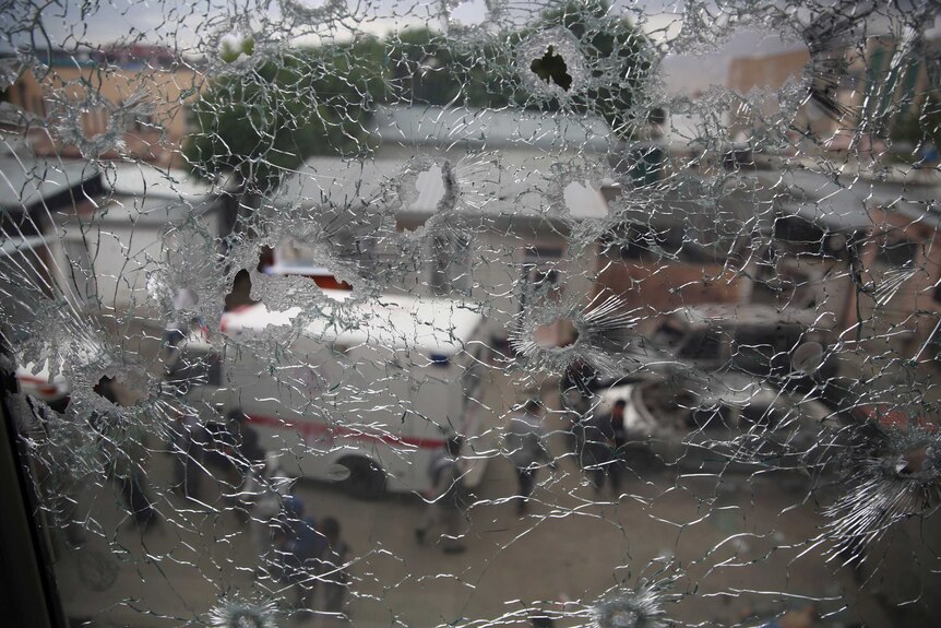 Afghan security officers are seen through the shattered window of a maternity hospital.