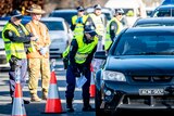 NSW police officers and a solider checking a queue of cars at a border.