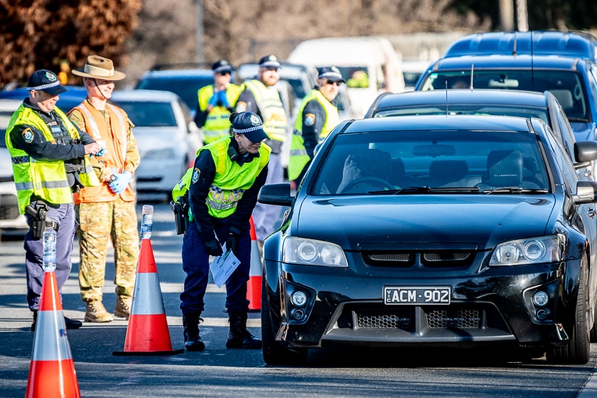 NSW police officers and a solider checking a queue of cars at a border.