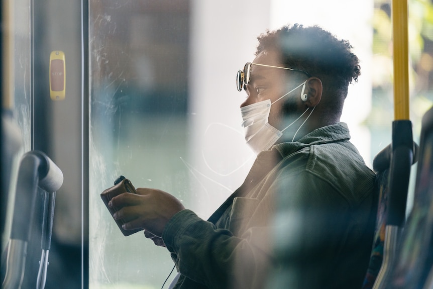 A man wearing a white face mask while aboard a Transperth bus within the city.