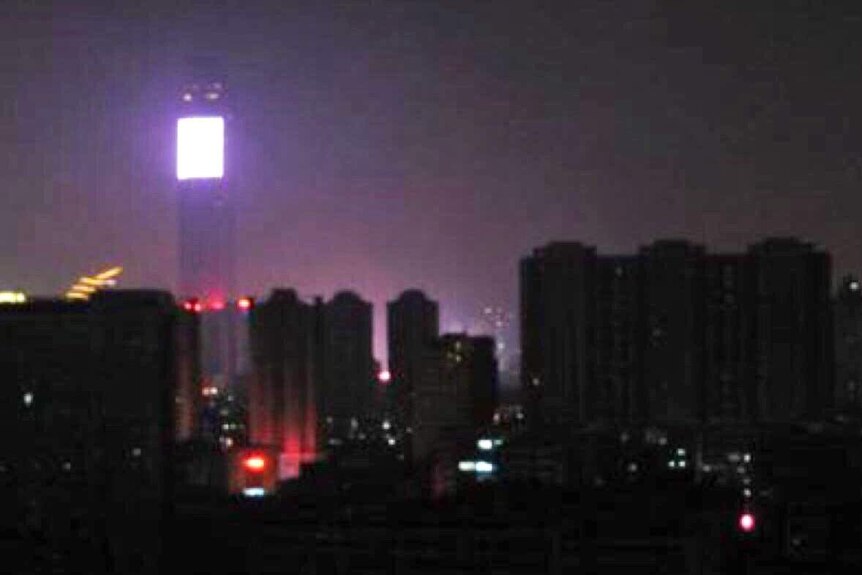 You view a grainy mobile image of a high-rises with no lights at night, with only one light source on the horizon.