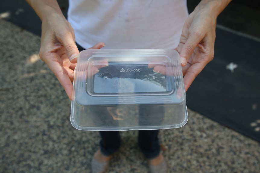 A plastic food container held upside down by two hands either side of it