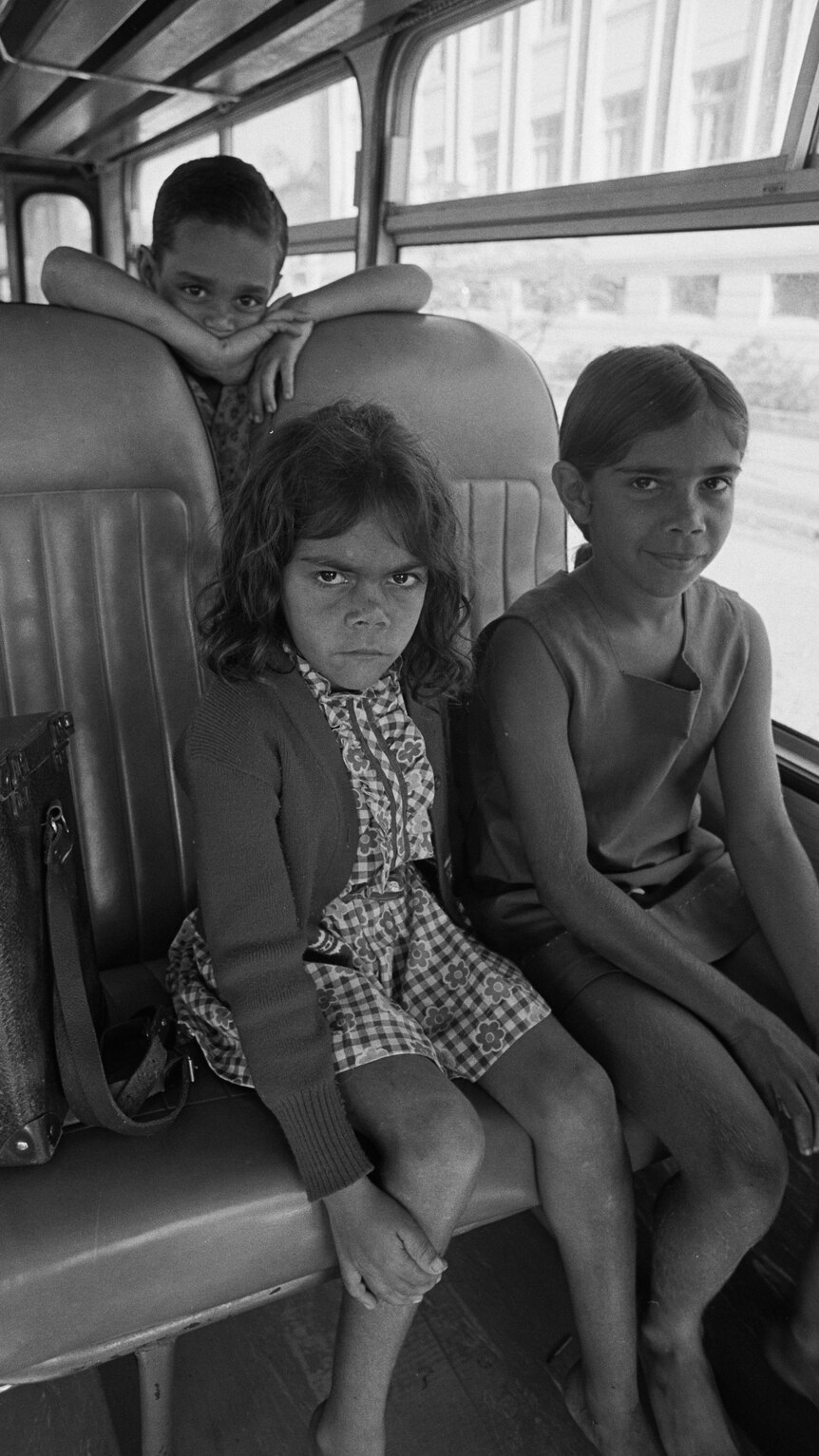 Two young girls and a young boy sitting on a bus.