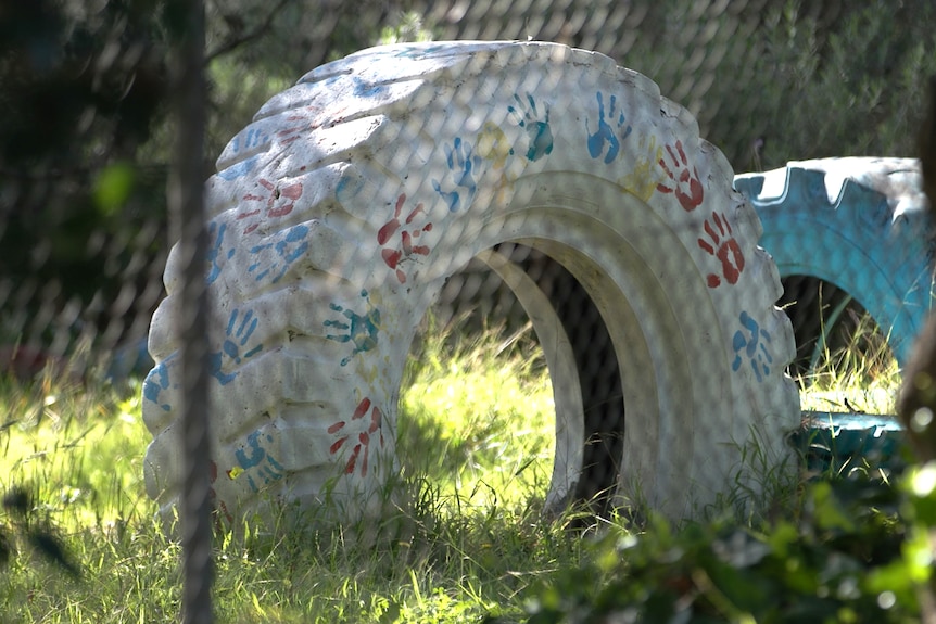 A large old tyre that has been converted to children's playground equipment. It is covered in painted hand prints.