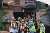 people stand next to and site inside a helicopter labelled 'hat-trick'