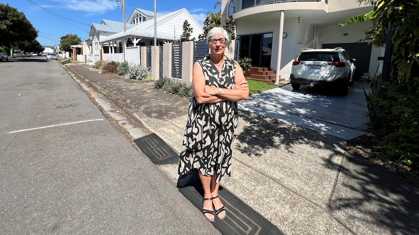 An elderly woman in a dress stands in front of her Newcastle home.