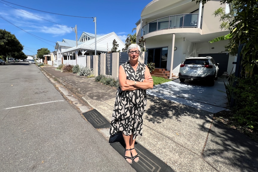 An elderly woman in a dress stands in front of her Newcastle home.