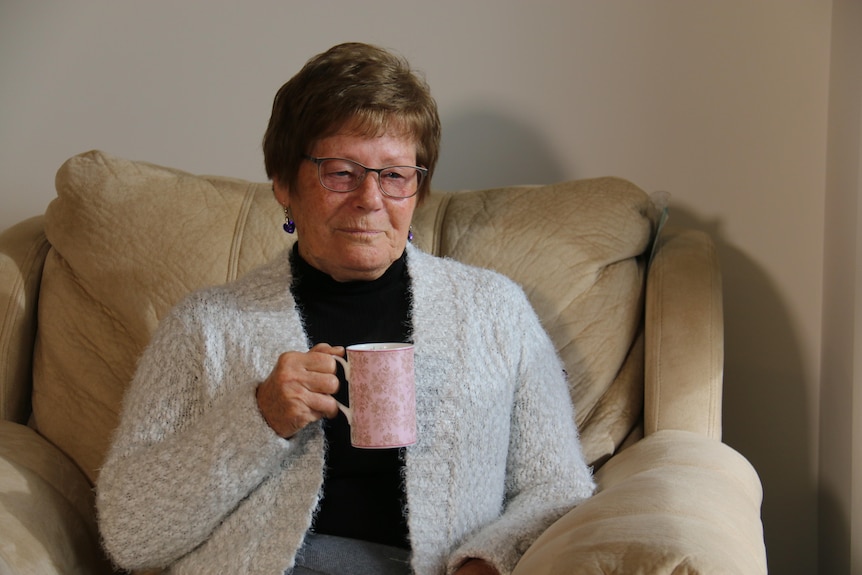 Diane sits and looks into the distance, holding a tea cup.