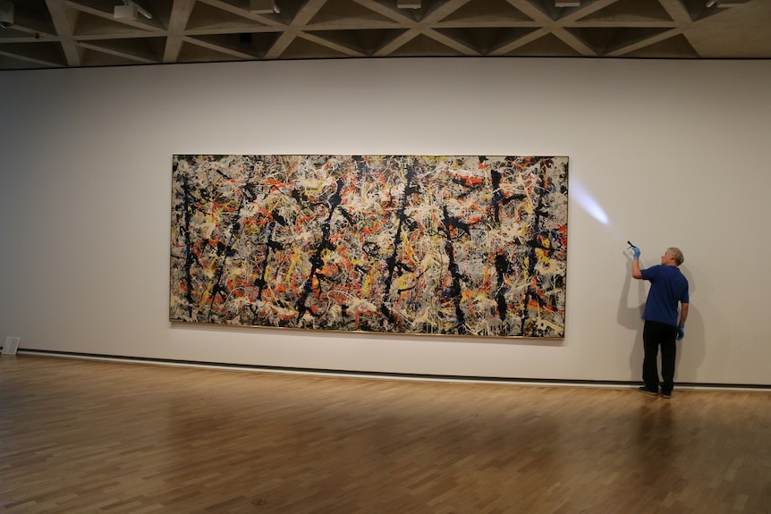 Staff member at the National Gallery of Australia shines a torch behind the Blue Poles artwork.