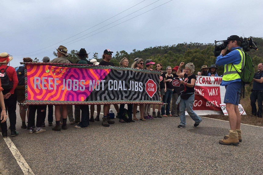 A group of people holding an anti-coal banner stand on the road outside the Abbot Point coal terminal.