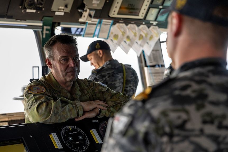 A man in military uniform speaks to another man inside a ship