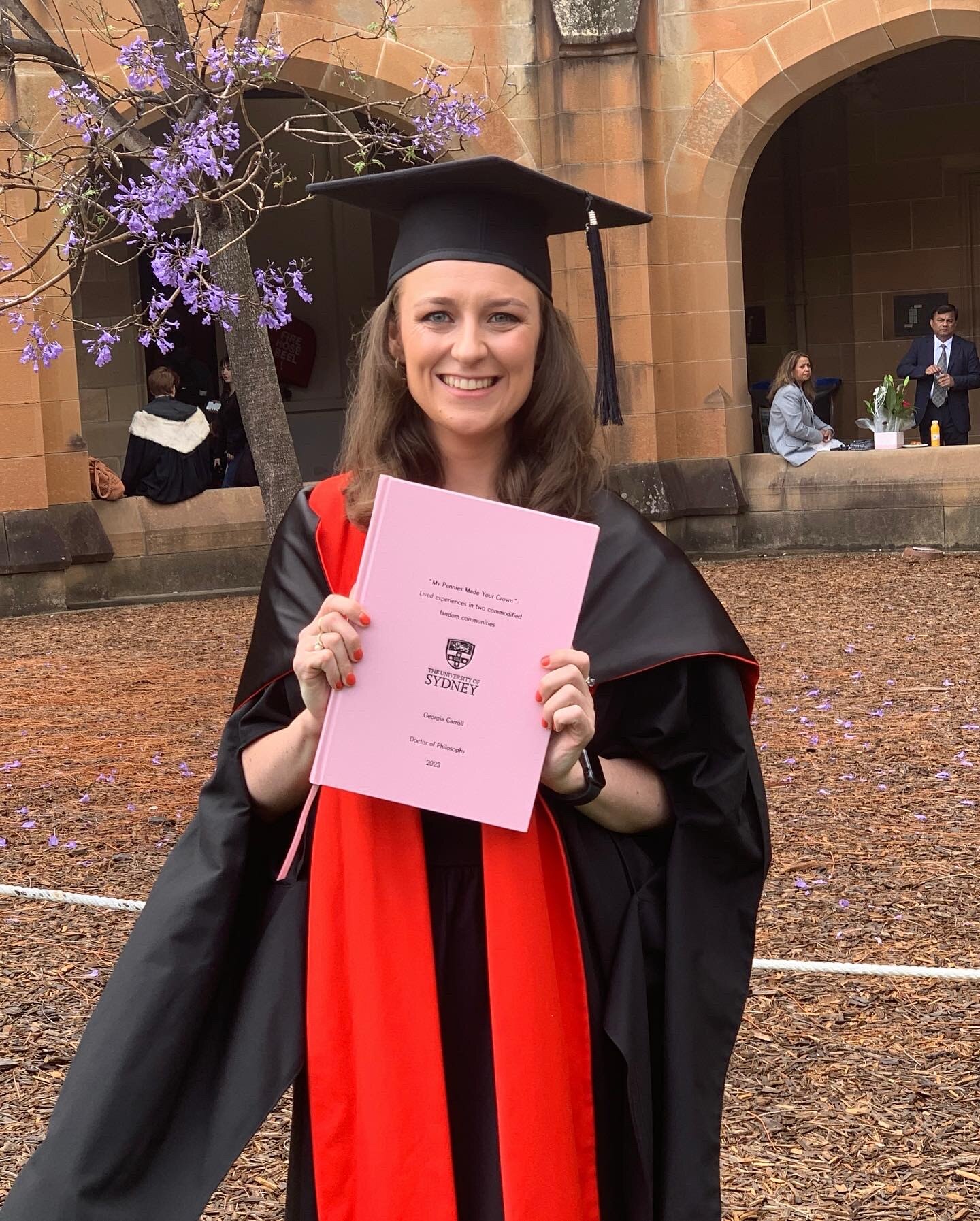 Picture of Dr Georgia Carroll in academic cap and gown, holding up her thesis.