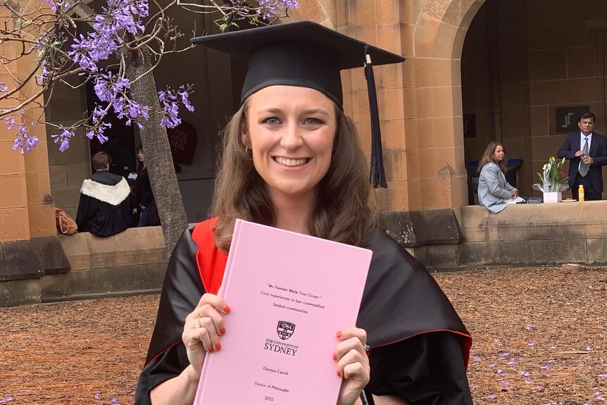 Picture of Dr Georgia Carroll in academic cap and gown, holding up her thesis.