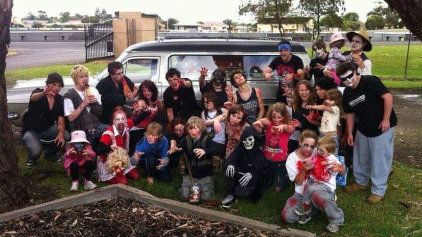 A group of people dressed as zombies standing in front of a hearse
