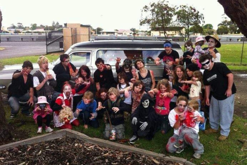 A group of people dressed as zombies standing in front of a hearse