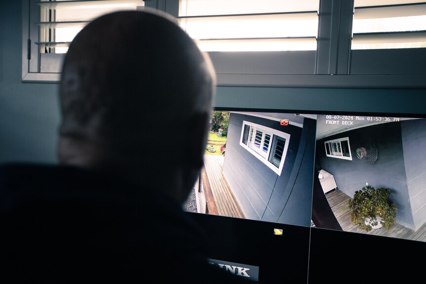 view from behind of a bald man watching security camera feeds