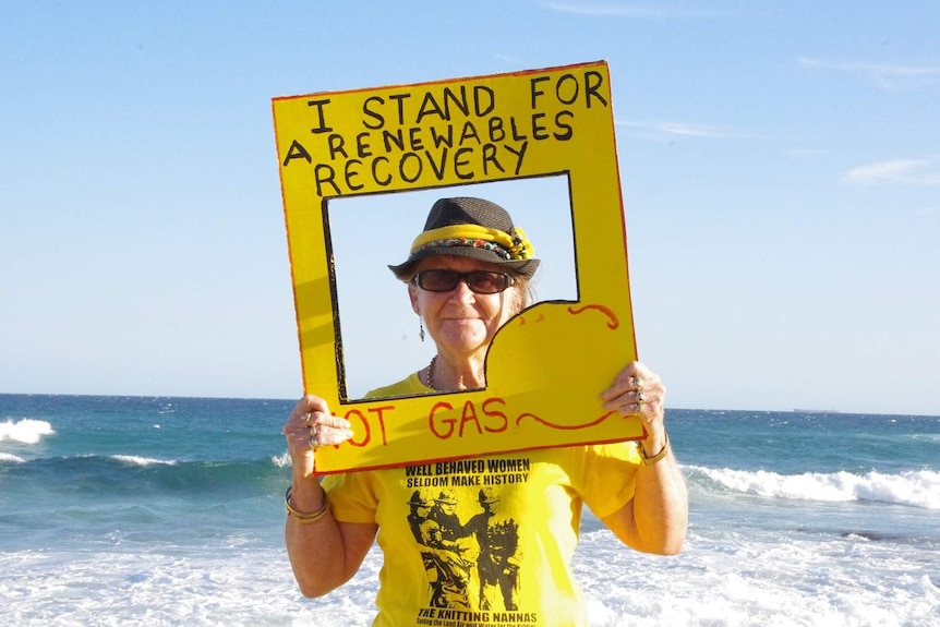 Julia Lee, dressed in yellow, holds up a sign that says "I stand for a renewables economy, not gas" at Bar Beach.