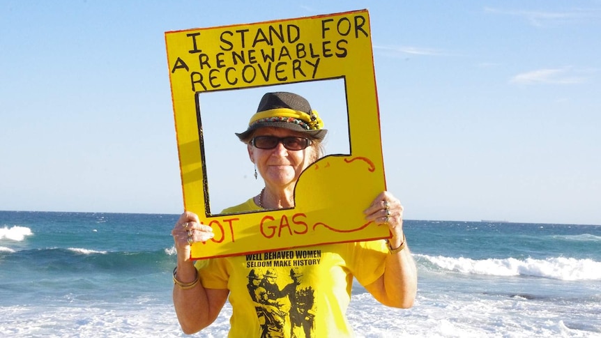 Julia Lee, dressed in yellow, holds up a sign that says "I stand for a renewables economy, not gas" at Bar Beach.