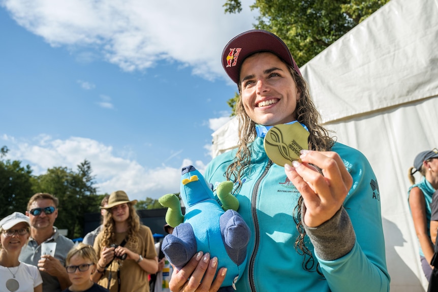 Jess Fox poses for a photo with her world championship gold medal, a hat and plushie