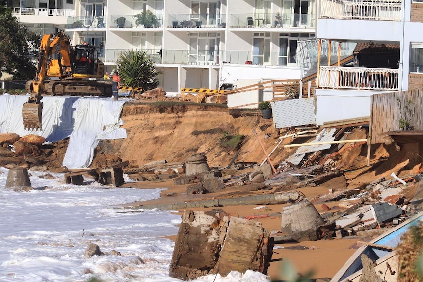 Heavy machinery lifts boulders into place at Collaroy Beach, with debris strewn across the beach.