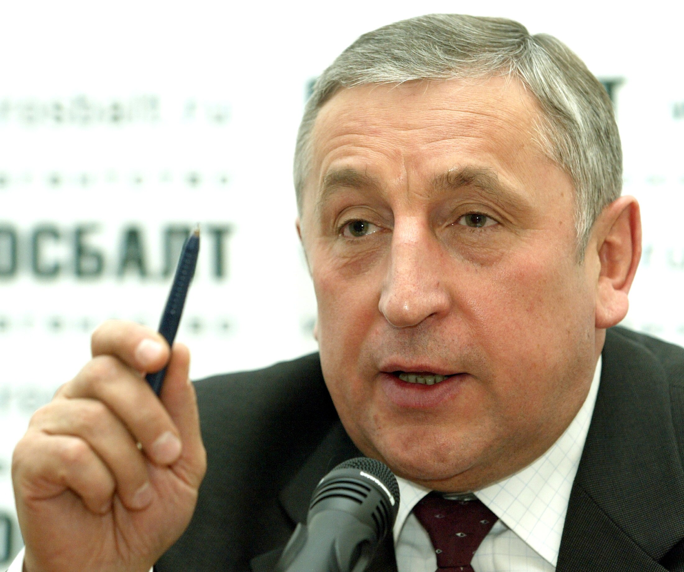 A man gestures while holding a pen in front of a desktop microphone