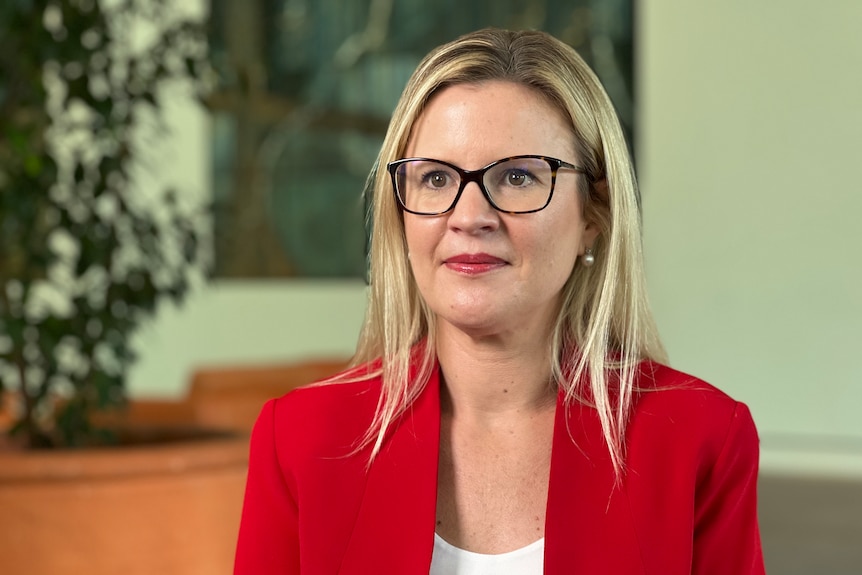 Woman with blonde hair wearing glasses and a red jacket.