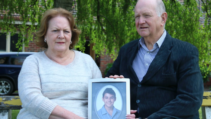 A man and a woman sit on a park bench holding a photo.