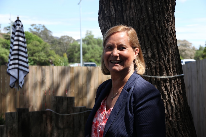 A blonde woman stands in the sun, beaming.